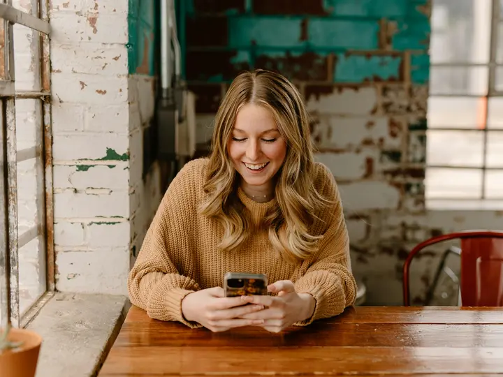 Woman at a cafe table smiling as she reads a welcome email on her phone
