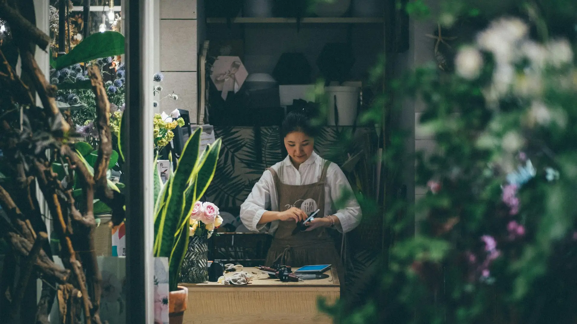 Florist working at the counter of her flower shop, seen through the shop window
