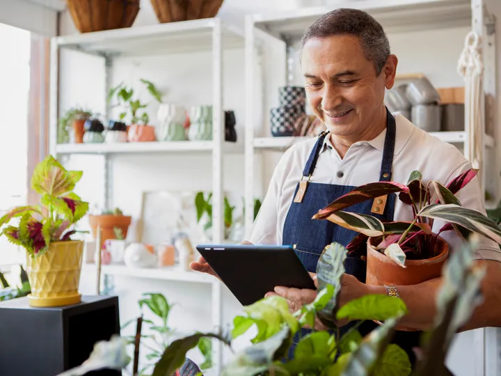 Plant shop owner smiling while checking orders on a tablet in his store