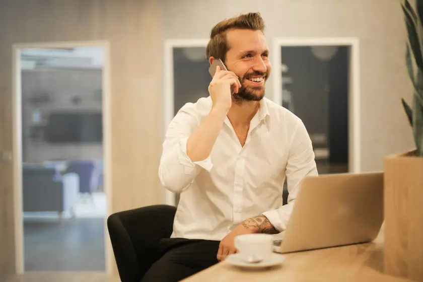 Smiling salesperson on a phone call with a new lead at his desk, laptop open