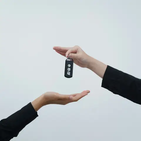 One hand passing a car key to another against a light background