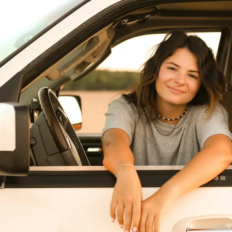 Email header photo: a smiling woman with long dark hair resting her arms on the open window of a white pickup truck