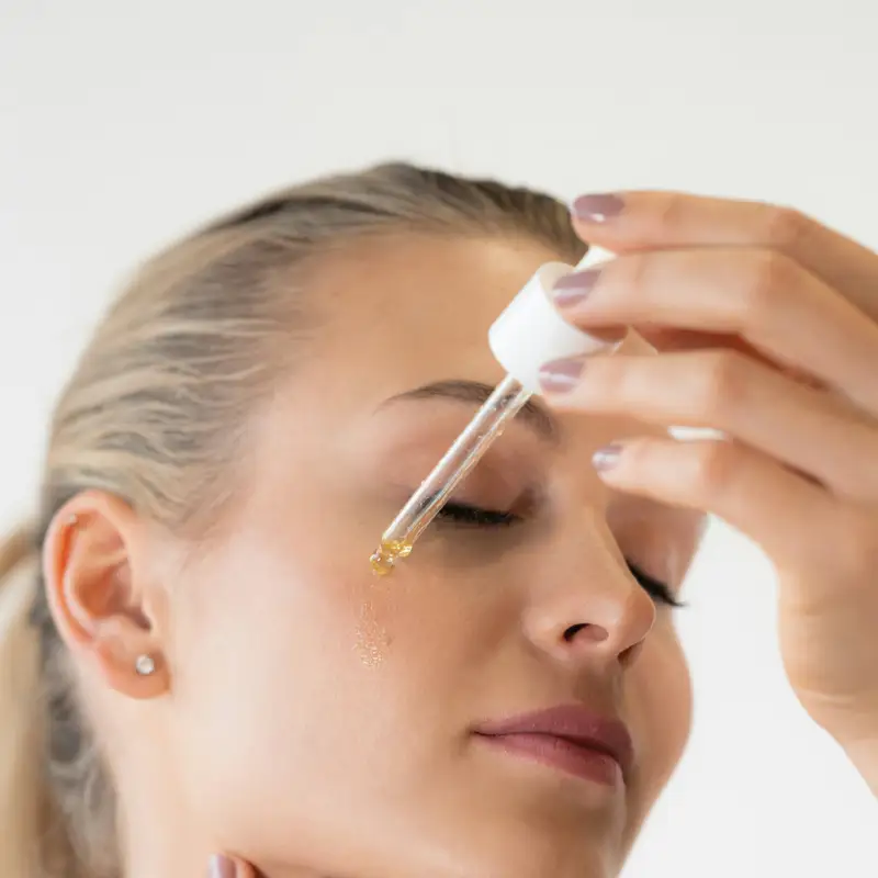 Email header photo: a woman with her eyes closed applies a drop of facial serum to her forehead from a glass dropper