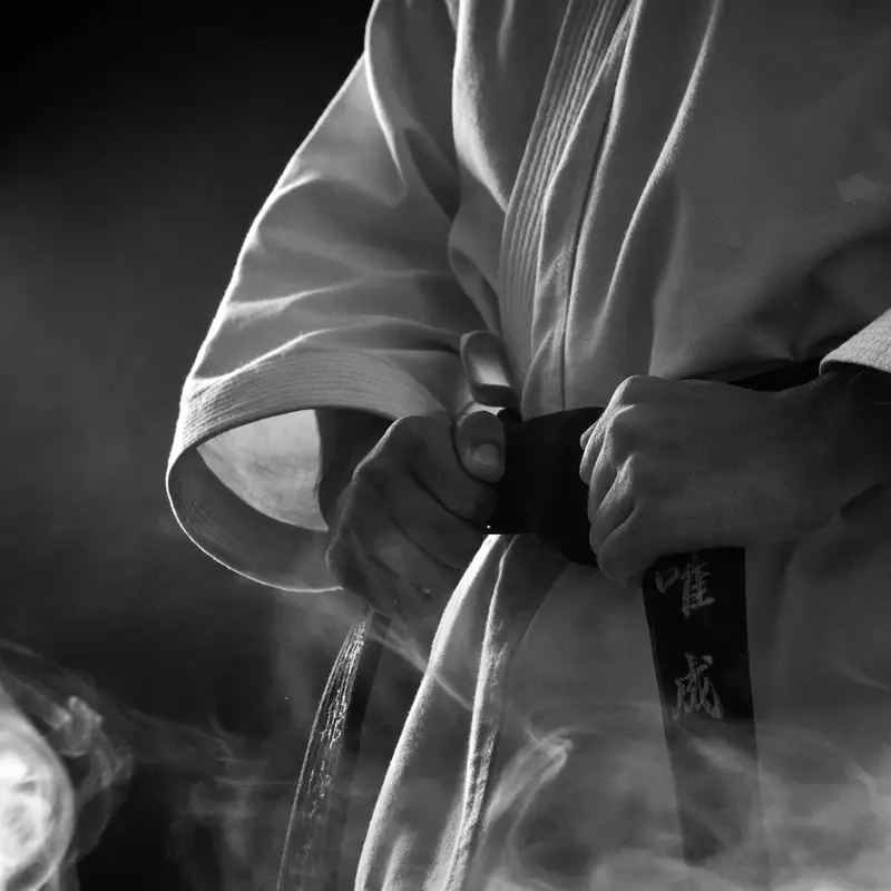 Email header photo: close view of a student in a white uniform tying an embroidered black belt, face out of frame