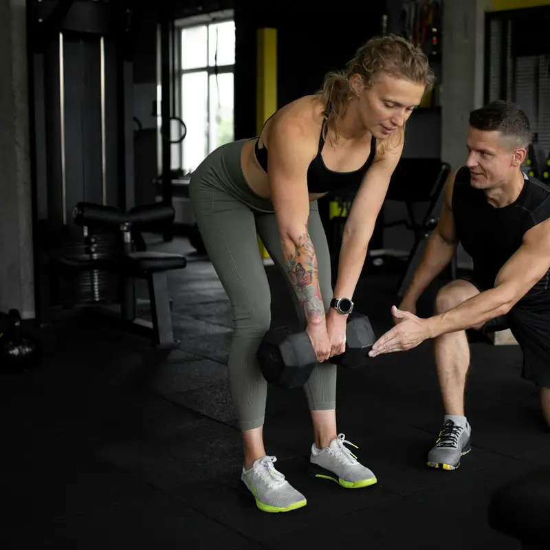 Email header photo: kneeling trainer guiding a woman through a dumbbell row during a one-on-one session