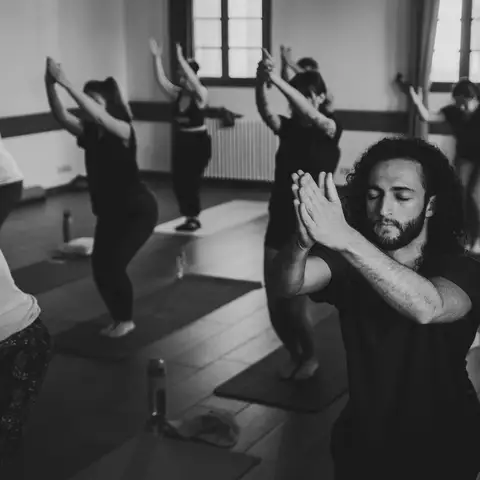 Black and white photo of a yoga class holding a bent-knee pose with arms raised and wrapped