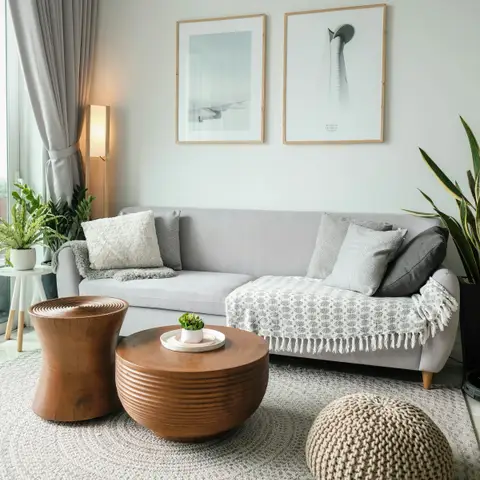 A light living room with a pale gray sofa, a woven rug, a round wooden coffee table and a knitted pouf