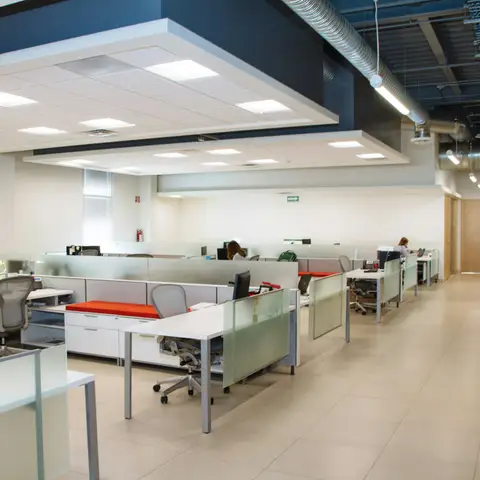 A bright open-plan office with rows of white desks, frosted glass partitions and a spotless tiled walkway