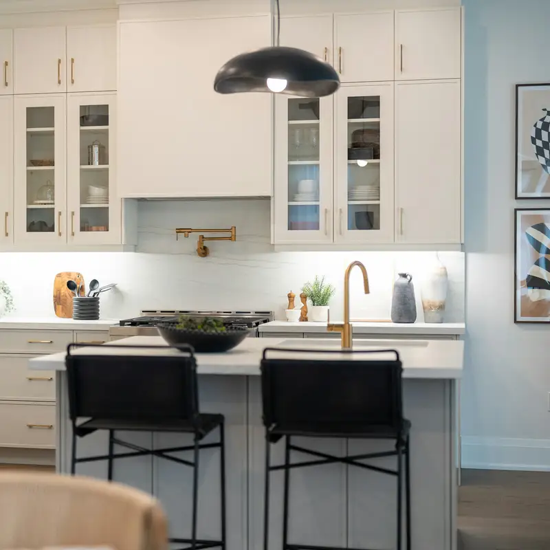 Email header photo: a spotless white kitchen with a clear island, black bar stools and a brass faucet under soft pendant light