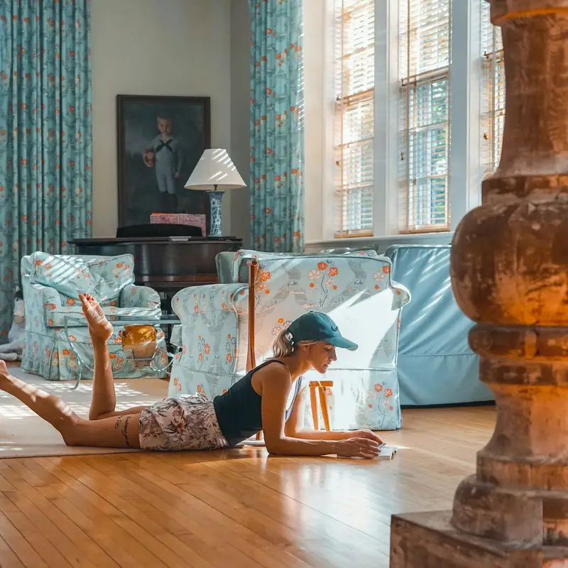 Email header photo: a woman in a cap lying on the wood floor of a bright, open living room, reading her phone in the afternoon sun