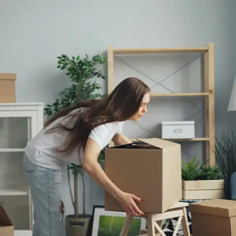 Woman lifting a moving box in a living room full of packed boxes
