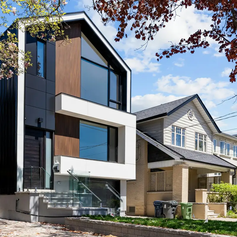 Email header photo: a new three-story modern home with dark metal siding and wood panels built beside an older house with a front porch