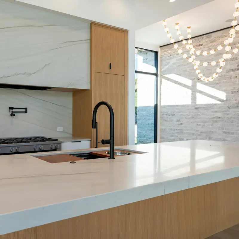 Email header photo: light oak cabinets around a white stone island countertop with a matching full-height stone backsplash and a black faucet