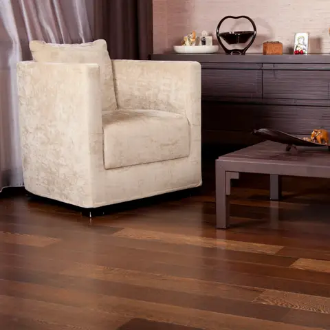 A sitting room with dark wide-plank hardwood floors under a cream armchair, a low wooden coffee table and a sideboard