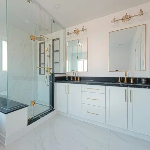 A remodeled bathroom with a glass walk-in shower and bench beside a white double vanity with brass fixtures