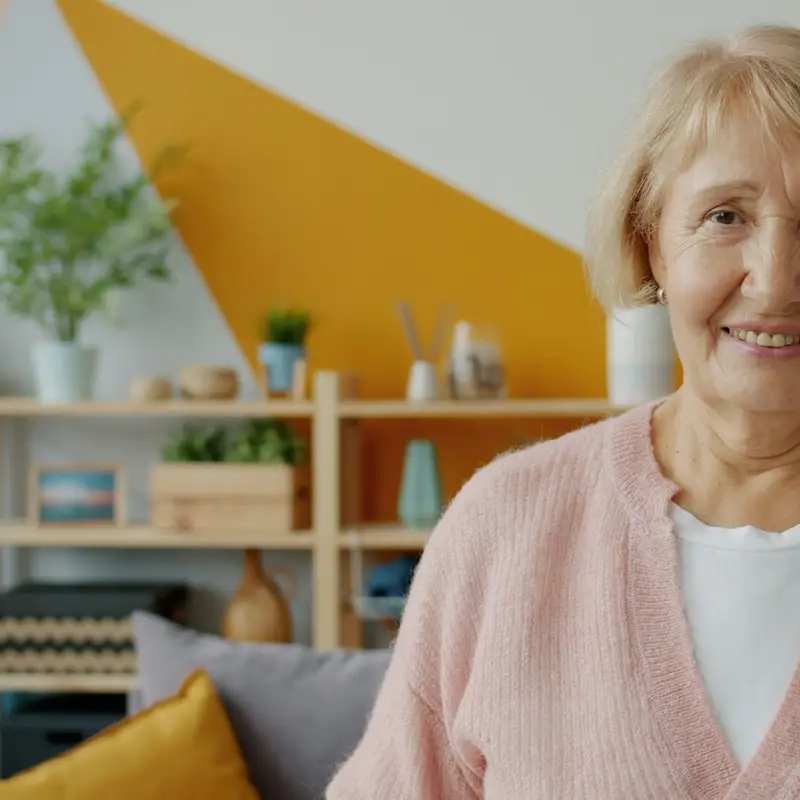 Email header photo: older woman with short blond hair in a pink cardigan smiling in a bright living room