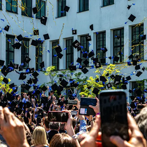 Graduates throwing their caps into the air in front of a white campus building while families take photos