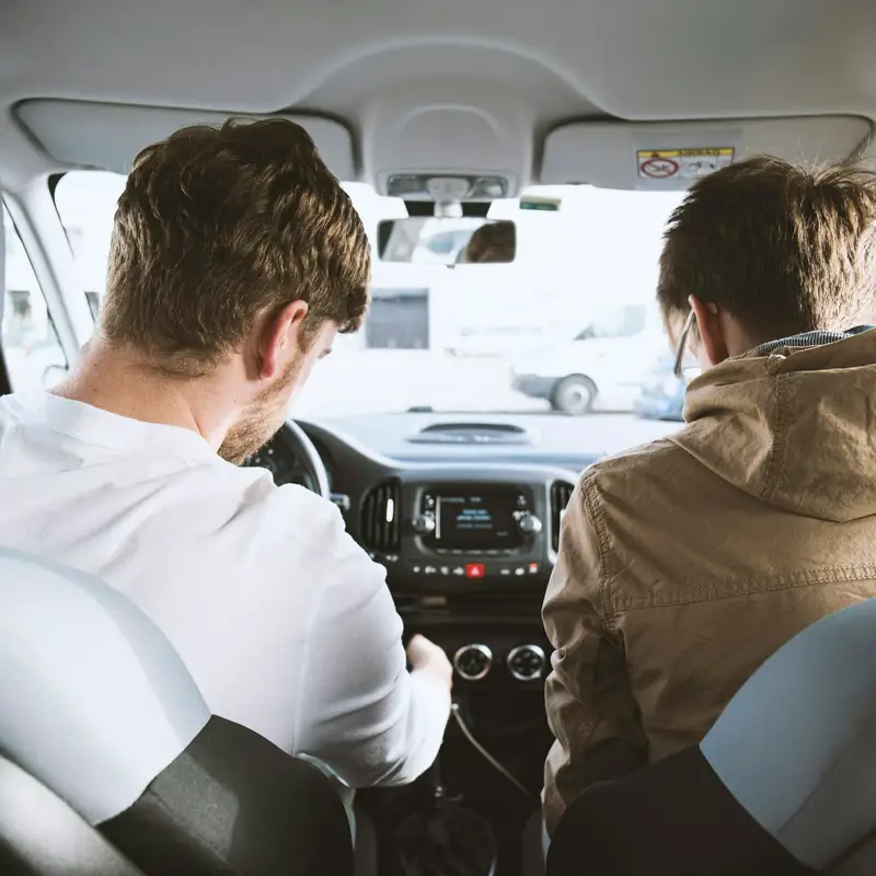 Email header photo: two men in the front seats of a car seen from the back seat, one at the wheel and one in the passenger seat, on a sunny day
