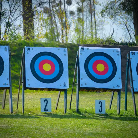 Four numbered archery targets standing in a row on a mown grass field in front of a wooded bank