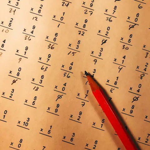 A red pencil resting on a multiplication drill worksheet filled in by hand