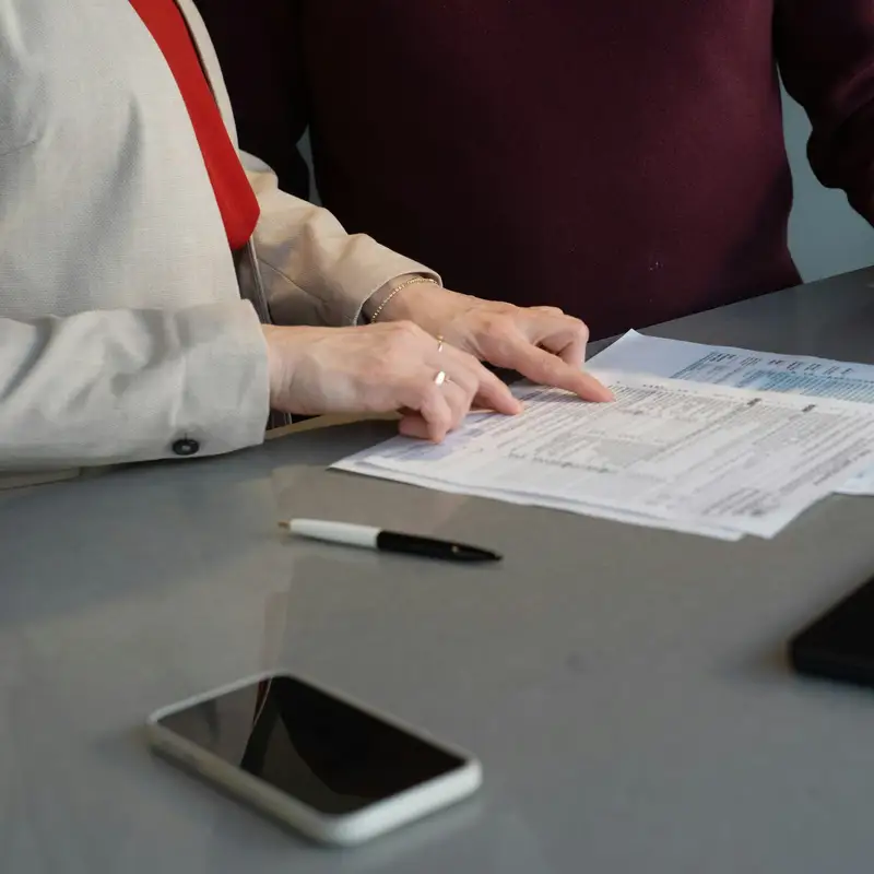 Email header photo: an advisor in a light blazer points to a line on printed forms while a client in a burgundy sweater looks on across a grey table