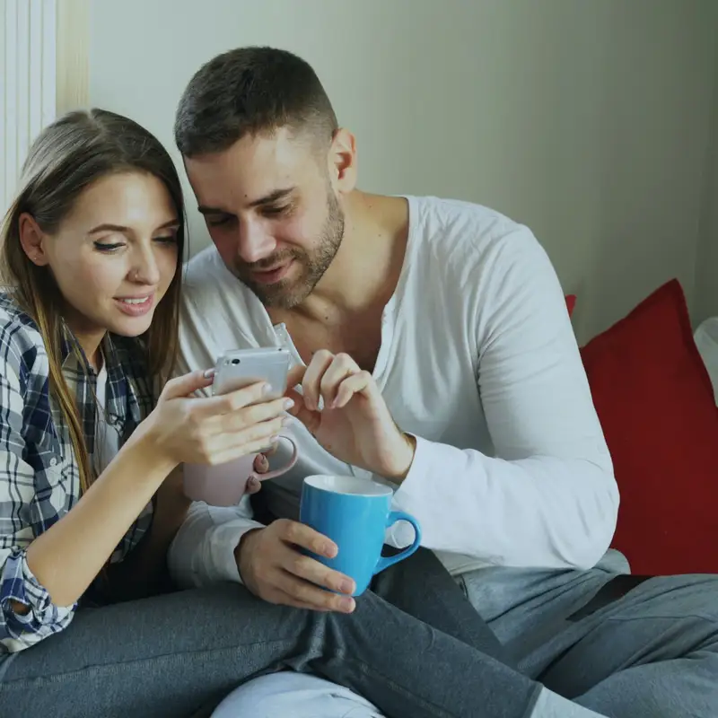 Email header photo: a young couple on a sofa at home looking at a phone together, one holding a coffee mug