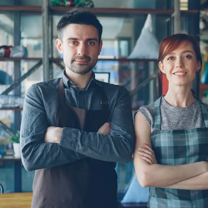 Email header photo: two restaurant owners in aprons stand with arms crossed in their dining room, smiling at the camera