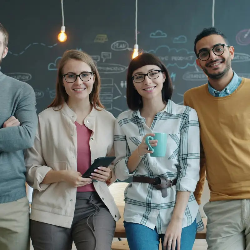Email header photo: four smiling coworkers stand together in a bright office with a chalkboard wall behind them