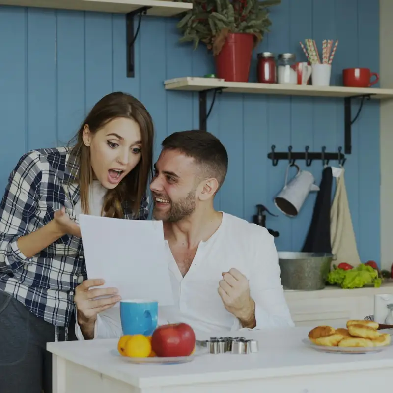Email header photo: a young couple in a bright kitchen read a letter together and react with surprise and delight