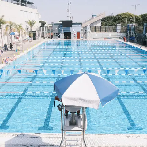 Outdoor public swimming pool with lap lanes and a lifeguard stand under a striped umbrella