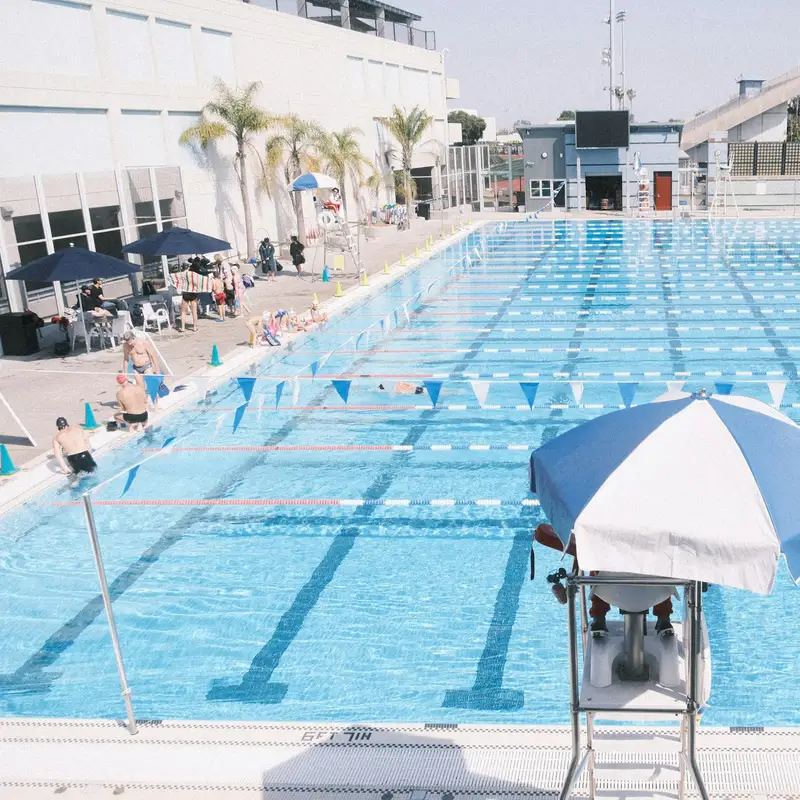 Email header photo: outdoor public swimming pool with lap lanes and a lifeguard stand under a striped umbrella