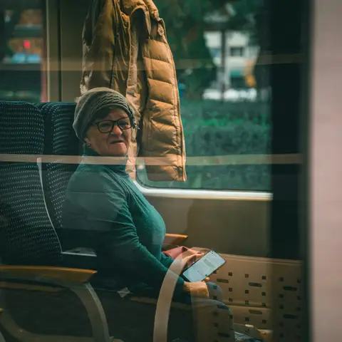 An older woman in a teal sweater and knit hat sitting by a train window with her phone in her hand