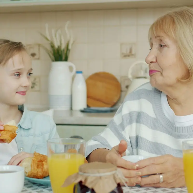 Email header photo: a grandmother and her granddaughter sharing breakfast with orange juice and croissants at a kitchen table