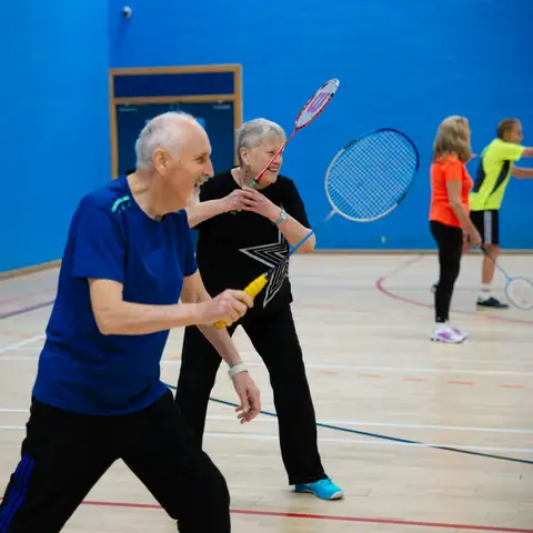 Older adults playing a lively game of badminton in a sports hall