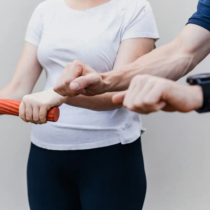 Email header photo: physical therapist guiding a patient through a grip exercise with a resistance bar