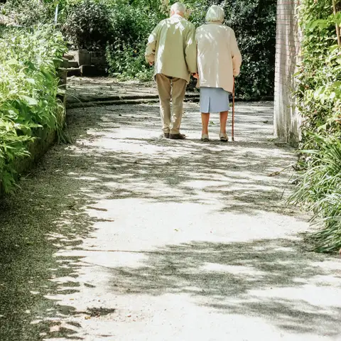 An older couple walking arm in arm along a sunlit garden path