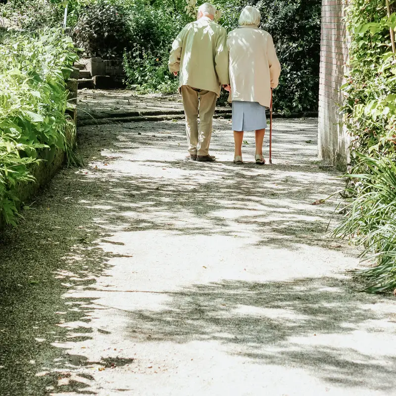 Email header photo: an older couple walking arm in arm along a sunlit garden path