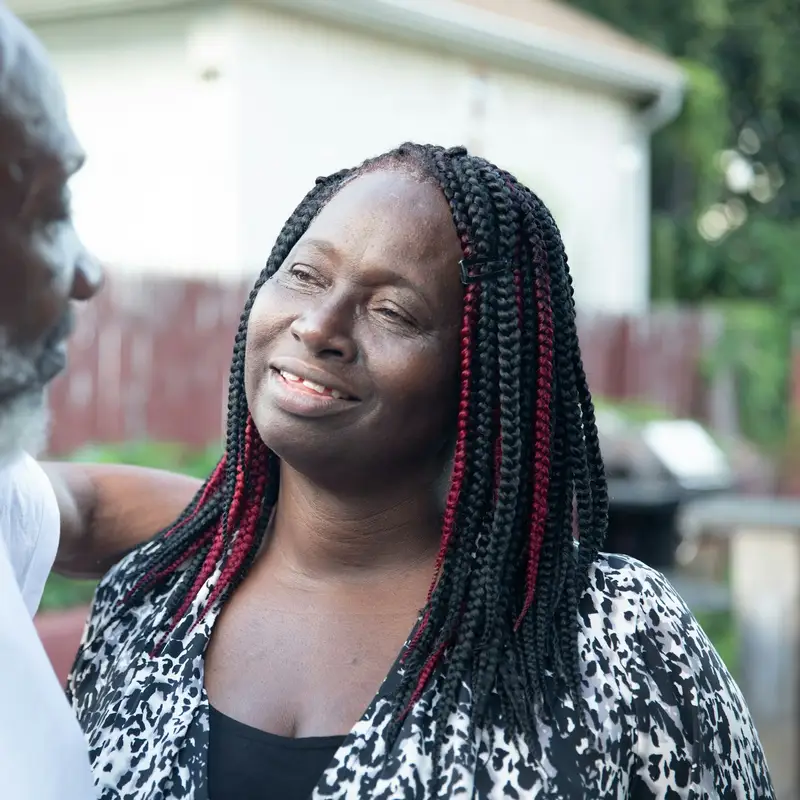 Email header photo: a smiling woman with braided hair looking at an older bearded man in a white t-shirt in a backyard