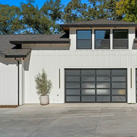 White board and batten house with two new dark glass-panel garage doors, potted plants and a fresh concrete driveway