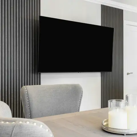 A flat screen TV mounted on a slatted wood panel wall above a dining table set with candles