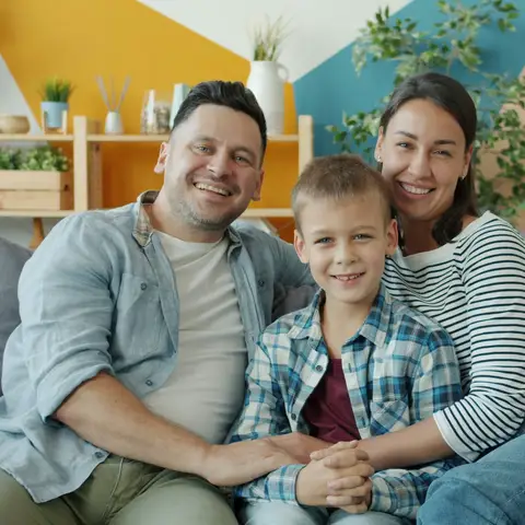 Smiling family of three sitting together on a living room sofa