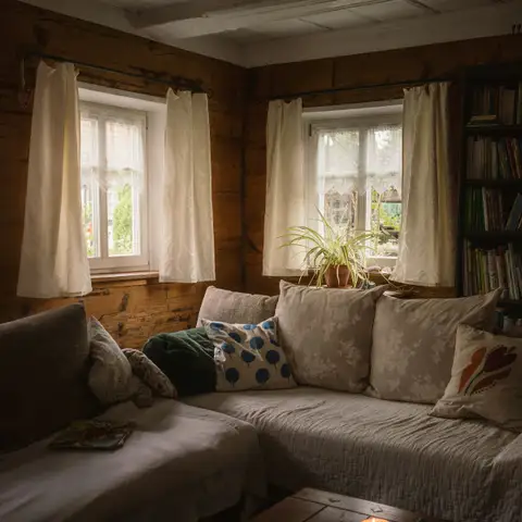 A cozy wood-paneled living room with a cushioned sofa, lit candles on a low table and white curtains on the windows