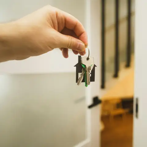 A hand holding up a set of house keys on a house-shaped key ring beside an open white front door