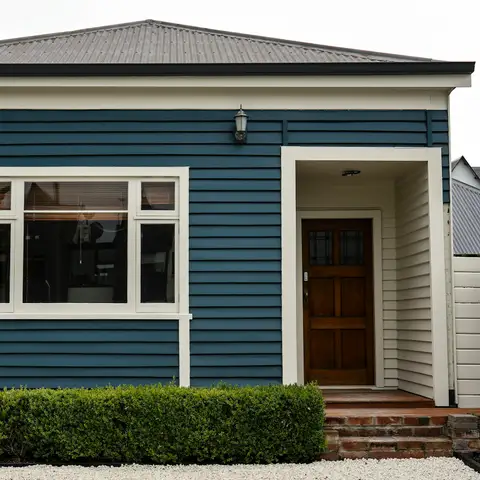 Small house with deep blue siding, crisp white trim, a wood front door and a trimmed hedge