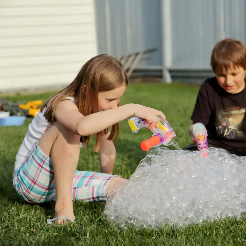 Email header photo: two children sitting on a green backyard lawn in the evening sun, playing with bubble toys beside a pile of foam bubbles