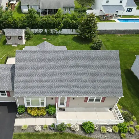 Aerial view of a single-family home with a clean grey shingle roof, a green lawn and flower beds