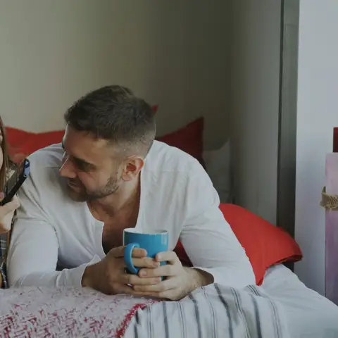 Couple relaxing in a bright bedroom with cups of coffee on a slow morning away
