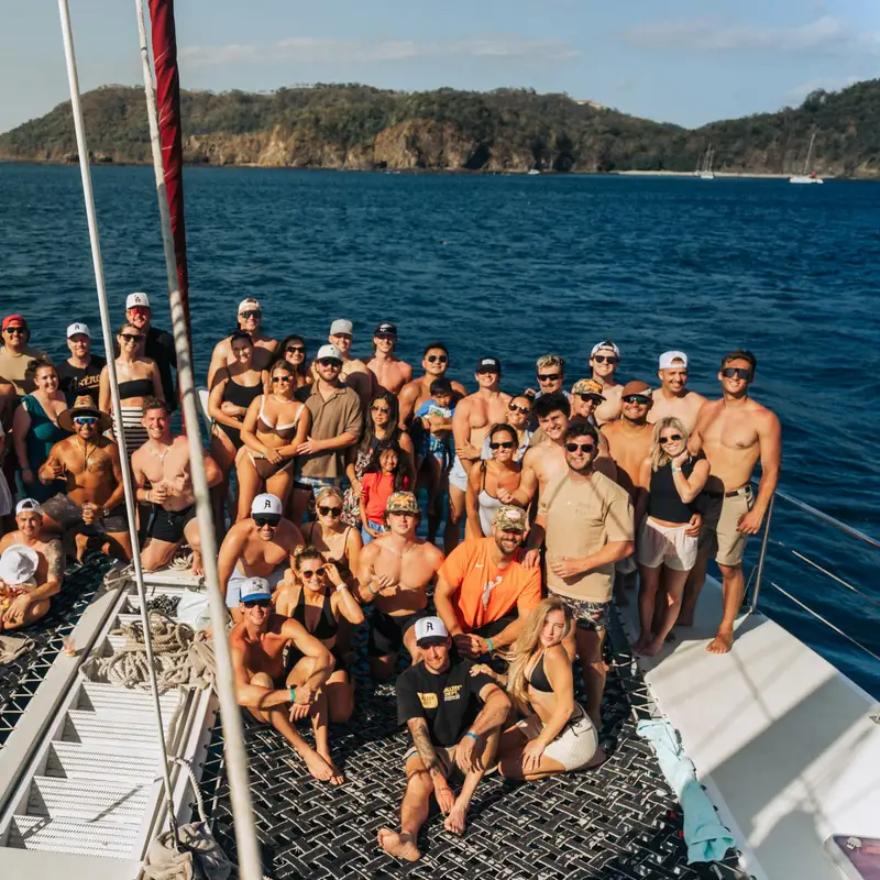 Email header photo: large group of travelers posing together on the deck of a catamaran in a sunny bay
