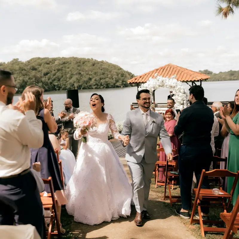 Email header photo: a newly married couple walking back up the aisle past cheering guests at an outdoor ceremony by the water