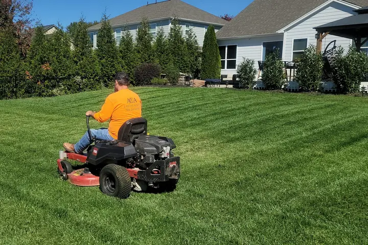 Landscaper riding a mower across a striped green lawn